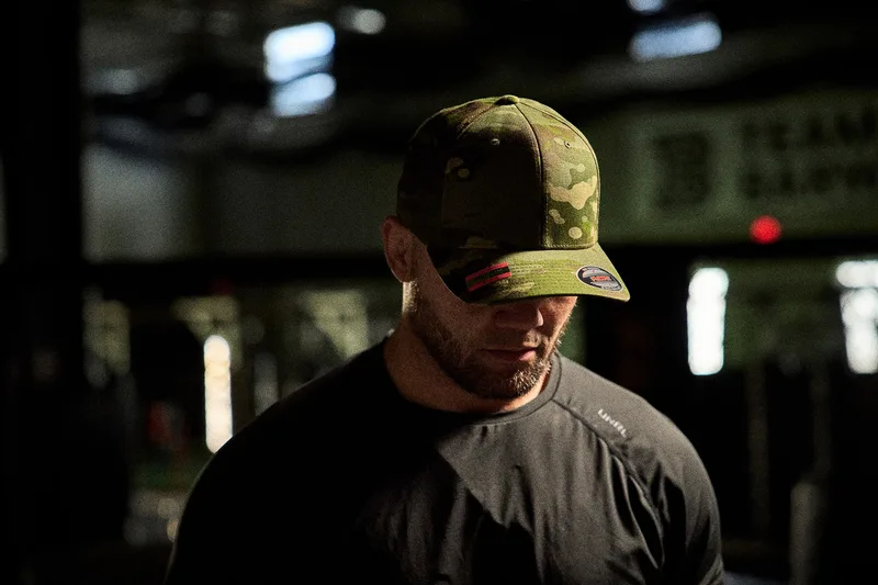 Mann mit Flexfit-Cap in Camouflage, dunkle Stimmung, im Hintergrund eine Halle (Kampagnenshooting Florida 2025)