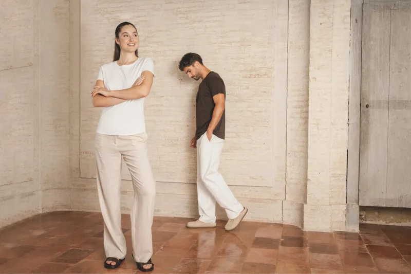 Frau in weißem und Mann in braunem T-Shirt in einem hellen Raum mit Backsteinwand und Terrakottaboden. Das Bild gehört zur Organic-Kollektion (Wechsel auf 100 %