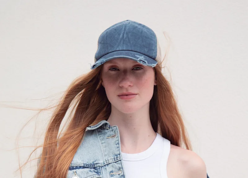 Junge Frau mit Jeans-Kappe, weißem Top und Jeansweste, die Haare im Wind, vor hellem Hintergrund. Es ist das og:image der K-up-Markenseite.