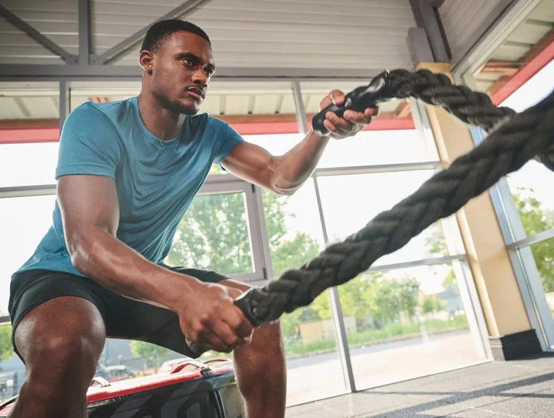 Mann in türkisem T-Shirt trainiert in einer hellen Halle mit Battle Ropes. Titelbild der Triblend-Reihe.