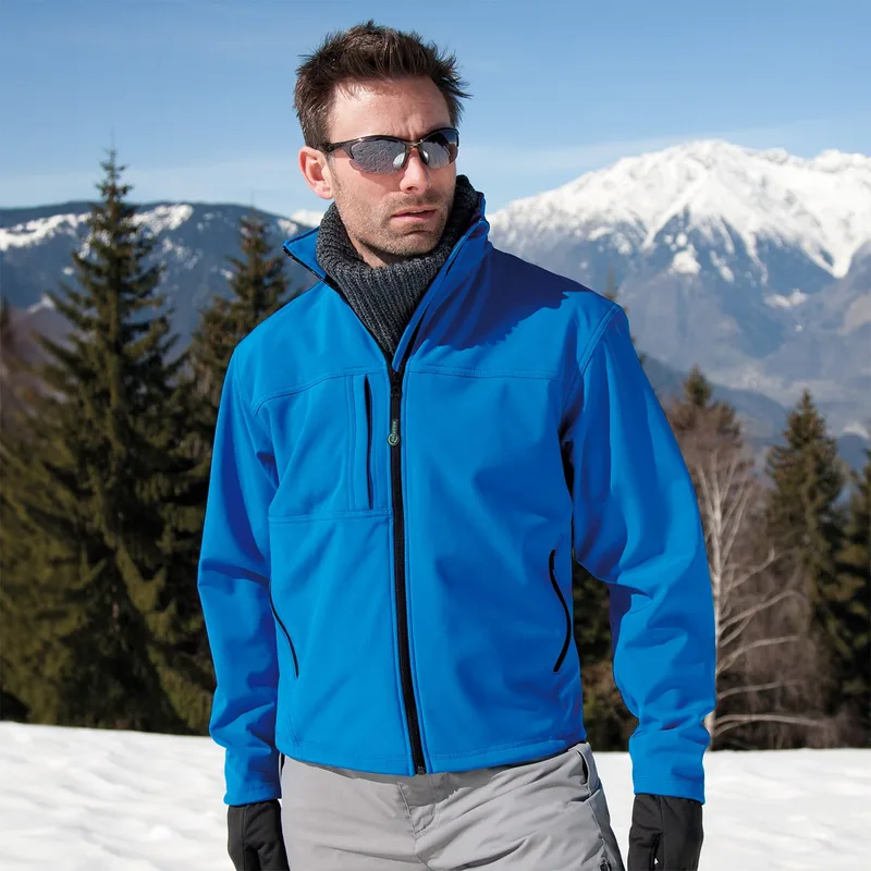 Mann mit Sonnenbrille in blauer Result-Softshelljacke vor verschneiten Bergen (quadratisch)