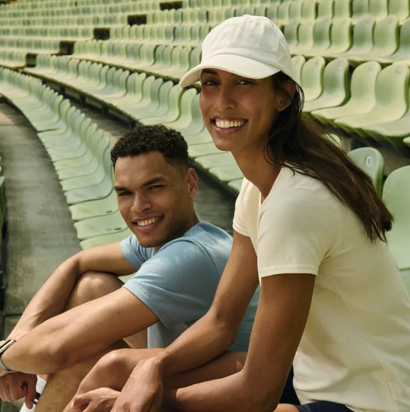 Junger Mann und Frau mit Cap sitzen lachend auf der Stadiontribüne