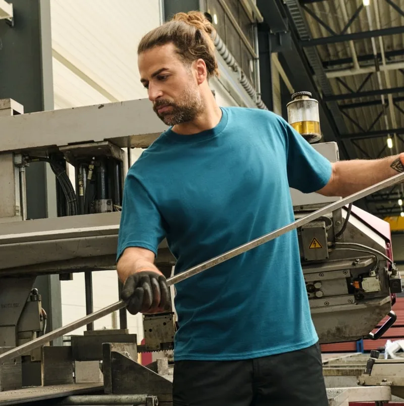 Mann in petrolfarbenem T-Shirt bei der Arbeit in einer Werkstatt