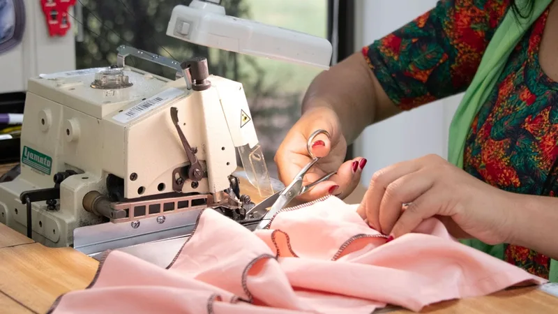 Näherin schneidet an der Nähmaschine Fäden an einem rosa Kleidungsstück (Nahaufnahme der Hände)