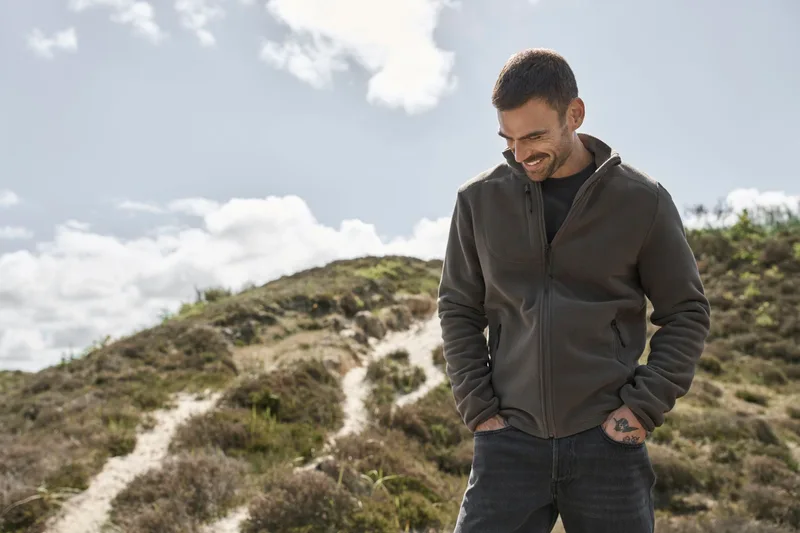Mann in brauner Jacke in einer Dünen- und Heidelandschaft unter Wolkenhimmel (ca. 29 MB)