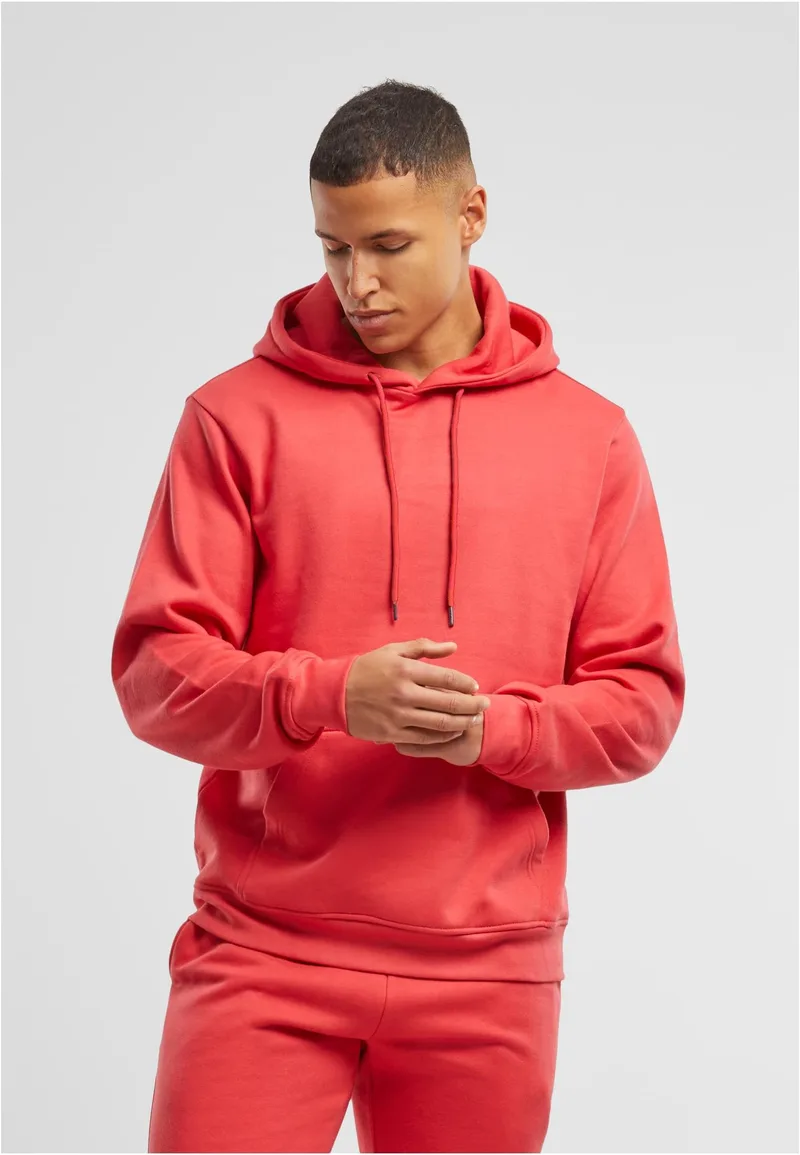 Mann in rotem Basic Hoody und Jogginghose, grauer Studiohintergrund