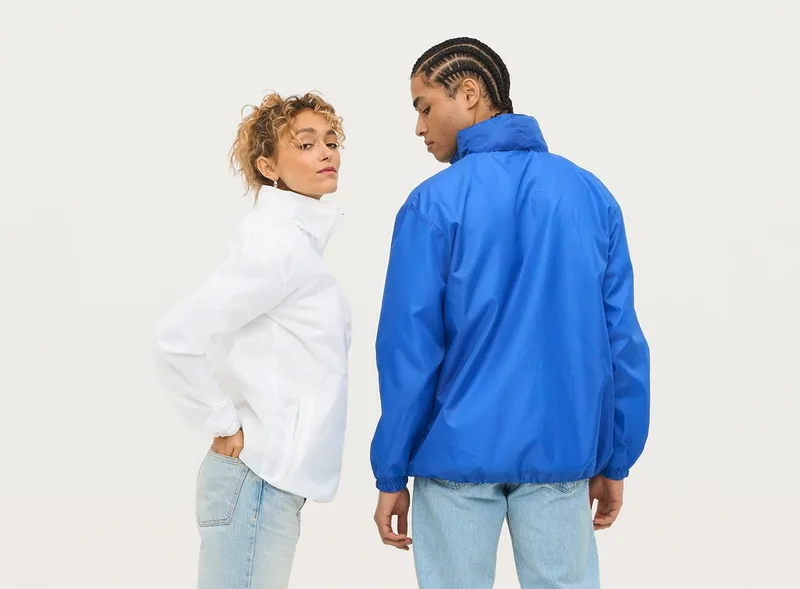 Frau in weißem Hemd und Mann in blauer Jacke, von hinten bzw. seitlich vor hellem Studiohintergrund.