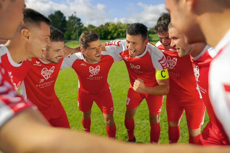 Fußballmannschaft in roten ERIMA-Trikots im Mannschaftskreis auf dem Platz