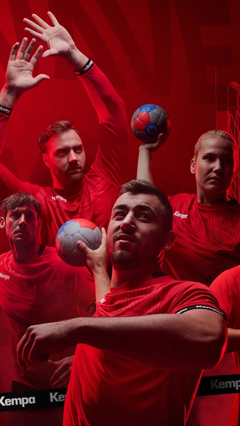 Handballteam in roten Kempa-Trikots mit Bällen, rote Kulisse (Hochformat)