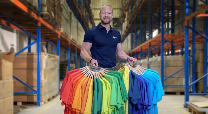 Mitarbeiter im Hochregallager hält einen Fächer aus Shirts in vielen Farben