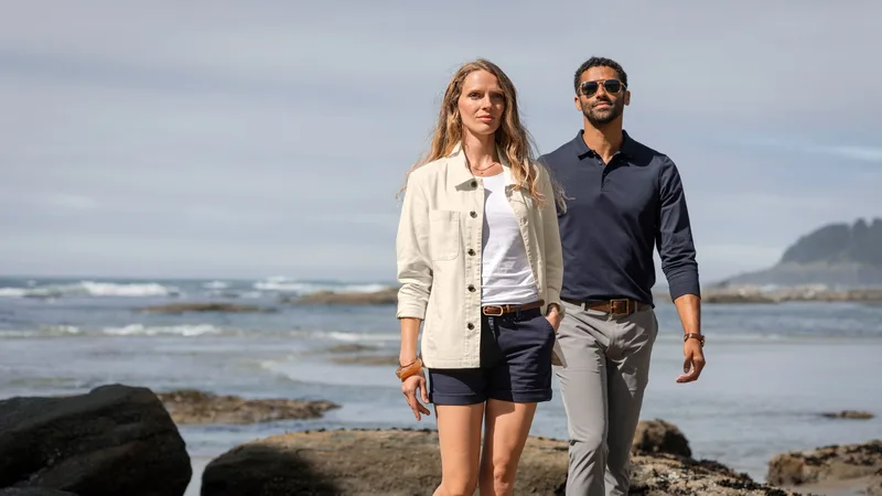 Paar in heller Jacke und dunklem Hemd spaziert an einem felsigen Strand