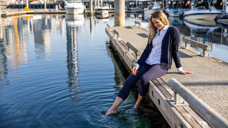 Frau in dunkelblauer Cutter-&-Buck-Jacke sitzt auf einem Bootssteg in einer Marina, die Füße im Wasser